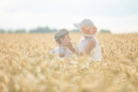 Photo for Portrait of happy boy and girl in hats standing in wheat field - Royalty Free Image