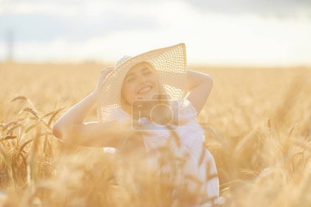 Téléchargez les photos : Portrait de femme heureuse en chapeau, posant dans le champ de blé - en image libre de droit