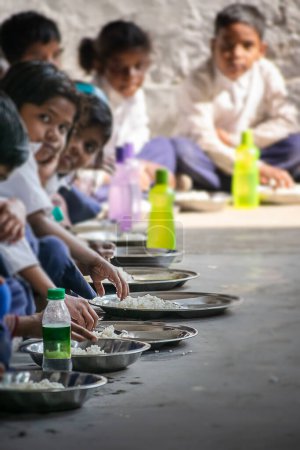 Téléchargez les photos : Des enfants assis en position assise en train de manger un repas de midi dans une école primaire gratuite du village de West Bengali, en Inde, dans le cadre du programme en cours de l'OMS, de l'UNICEF, de l'UNESCO. - en image libre de droit