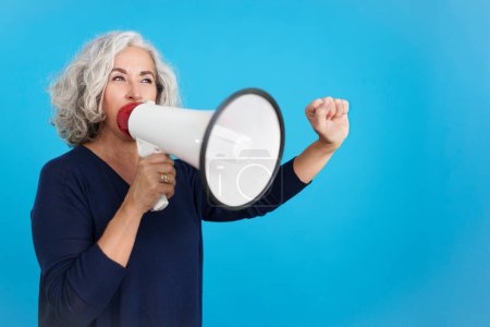 Photo for Studio portrait with blue background of an upset mature woman protesting with megaphone - Royalty Free Image