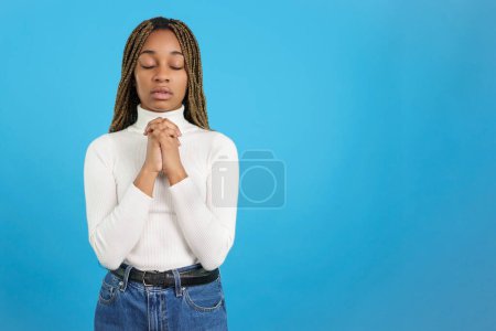 Foto de Studio portrait with blue background of an african woman with eyes closed and folded hands in prayer - Imagen libre de derechos