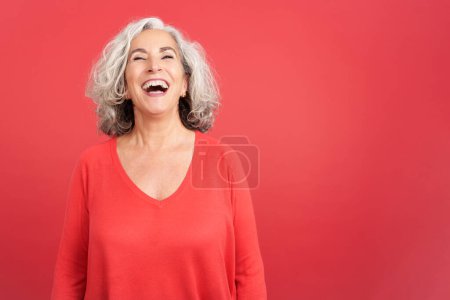 Photo for Studio portrait with red background of a mature woman in red shirt laughing while standing - Royalty Free Image