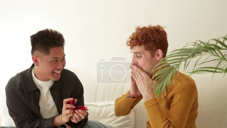 Téléchargez les photos : Vidéo au ralenti d'un homme gay demandant à son partenaire de l'épouser sur le canapé à la maison - en image libre de droit