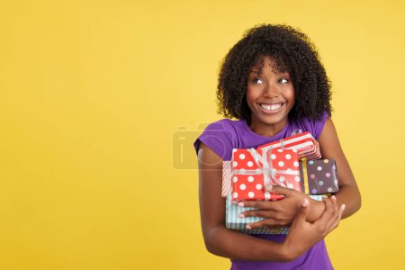 Téléchargez les photos : Femme drôle et gourmande avec afro cheveux tenant cadeaux en studio avec fond jaune - en image libre de droit