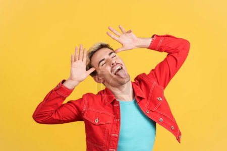 Téléchargez les photos : Gay l'homme grimacing et blague avec la langue dehors dans studio avec jaune fond - en image libre de droit
