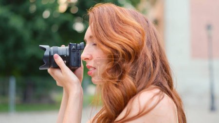 Close up profile of a a beauty red-haired woman taking a photo outdoors