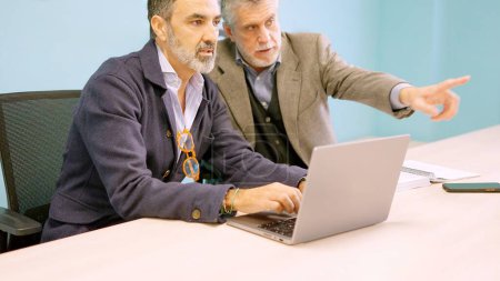 Two mature partners discussing which workers they will dismiss in front of the computer