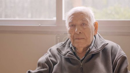 Hombre de edad mirando en serio a la cámara sentado en un geriátrico