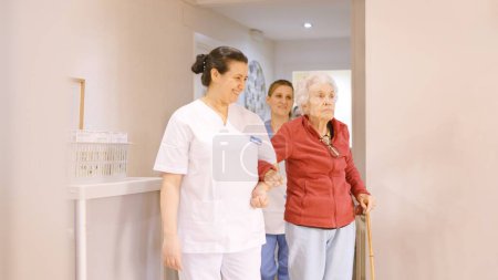 Foto de Cuidadores que sostienen el brazo de personas mayores mientras caminan en un geriátrico - Imagen libre de derechos