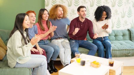 Grupo de amigos celebrando algo que están viendo en la televisión mientras toman una copa en casa