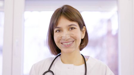 Doctora en bata de laboratorio sonriendo a la cámara en la clínica
