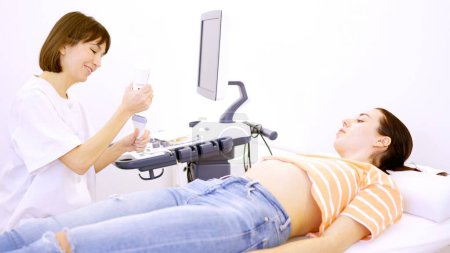 Doctora preparándose para realizar un ultrasonido a una mujer embarazada