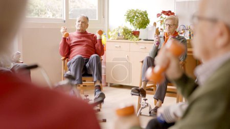 Group of senior men and women exercising in a nursing home using dumbbells and pedals
