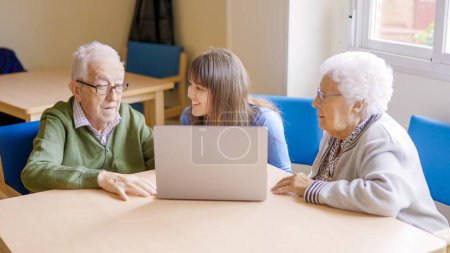 Téléchargez les photos : Petite-fille aidant ses grands-parents à utiliser l'ordinateur portable en gériatrie - en image libre de droit