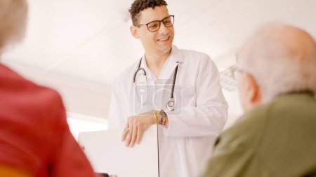 Foto de Médico gay escribiendo datos en un informe médico hablando con personas mayores - Imagen libre de derechos