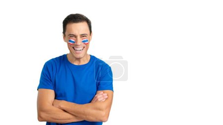 Man standing with tahi flag painted on face smiling with arms crossed