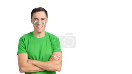 Hombre de pie con bandera nigeriana pintado en la cara sonriendo con los brazos cruzados