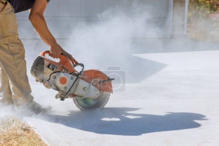 Construction worker cuts with working diamond bladed cut off saw to concrete paving sidewalk
