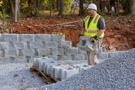Téléchargez les photos : Bâtiment mur de soutènement avec des blocs de soutènement sur une nouvelle propriété est fait par le travailleur de la construction - en image libre de droit