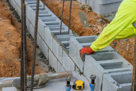 Photo for Bricklayer construction worker putting down another row of cement blocks in construction site - Royalty Free Image
