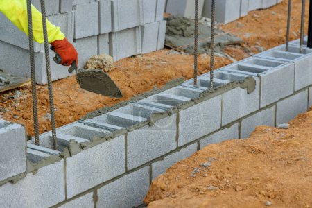 Photo for Bricklayer mason, is laying mounting for wall of concrete blocks that will be used as part building project - Royalty Free Image