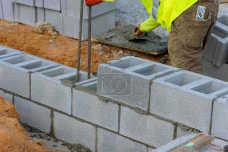 Photo for Bricklayer construction worker is laying down another row of cement blocks in construction site - Royalty Free Image