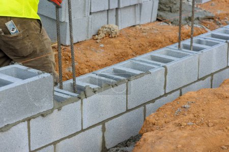 Téléchargez les photos : Mise vers le bas de la deuxième rangée de blocs de ciment par le travailleur de la construction de maçon sur le chantier - en image libre de droit