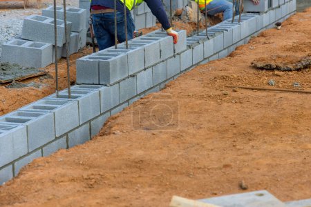 Photo for Worker placing cement blocks along another row of bricks in bricklaying construction site - Royalty Free Image