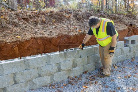 Mann ebnet Werkzeug beim Bau von Betonklotz-Stützmauer auf neuem Grundstück, das gebaut wird