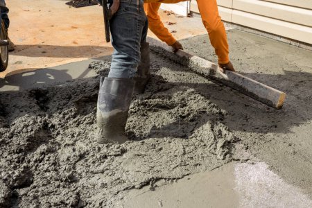 Foto de Los trabajadores construyen nueva acera adyacente a la casa vertiendo cemento en la casa lateral como parte del proceso de construcción - Imagen libre de derechos