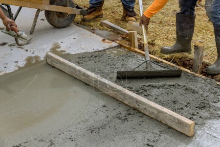 Bauarbeiter gießen Zement auf Hausseite, um einen zusätzlichen neuen Bürgersteig zu schaffen
