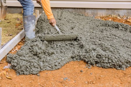 Photo for On side of house, construction workers pour cement to create an additional sidewalk as part renovation project - Royalty Free Image
