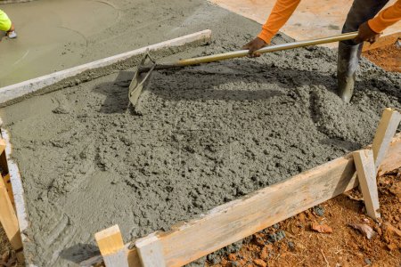 Téléchargez les photos : Il y a des travailleurs de la construction versant du ciment sur le côté de la maison afin de créer un nouveau trottoir - en image libre de droit