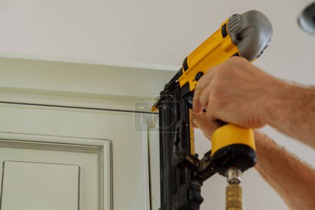Photo for Carpenter brad using nail gun to Crown Moulding on kitchen cabinets framing trim, with the warning label that all power tools have on them shown illustrating safety concept - Royalty Free Image
