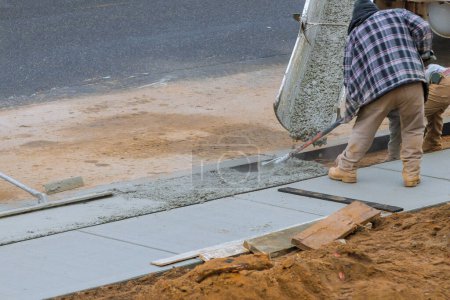 Téléchargez les photos : Les travailleurs versent du ciment sur le côté de la maison afin de créer un nouveau trottoir - en image libre de droit