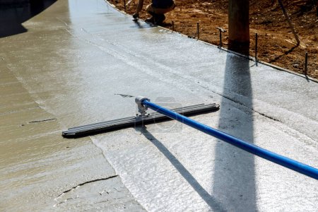 Téléchargez les photos : Worker is holding steel fresno trowel and smoothing out newly poured sidewalk on wet concrete in where construction taking place - en image libre de droit