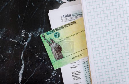 On desk 1040 individual income tax form, pen calculator, and dollar bills, tax return stimulus check