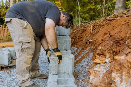 Téléchargez les photos : On construction site of construction worker was installing concrete block for retaining wall next to new house - en image libre de droit