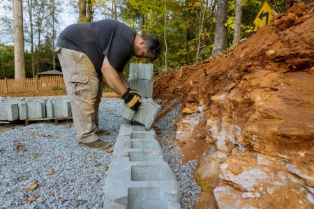 Téléchargez les photos : Construction worker was installing concrete block for retaining wall near new home in construction site - en image libre de droit