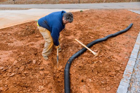 Photo for During major rainfall worker digs trench so as to lay drainage pipe for collect rainwater - Royalty Free Image