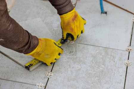 Photo for As contractor prepares to lay ceramic tiles on floor he measures tiles prior for cutting them - Royalty Free Image