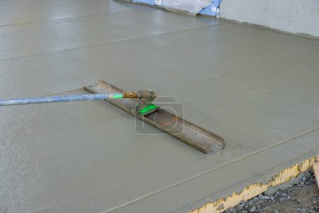 Photo for Worker was pouring concrete sidewalk using long trowel on wet cement surface he was leveling - Royalty Free Image