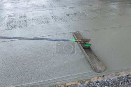 Photo for On wet cement sidewalk construction worker use long trowel to level concrete he was pouring - Royalty Free Image