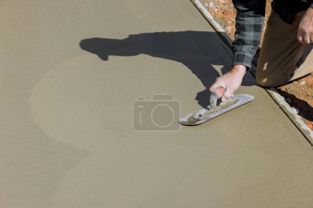 Téléchargez les photos : Après que le béton a été versé plâtre travailleur sol en béton humide de ciment avec l'aide de truelle - en image libre de droit