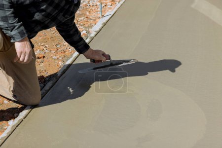 Téléchargez les photos : C'est le travail des travailleurs de plâtrer le sol en béton humide en ciment à l'aide d'une truelle après le coulage du béton - en image libre de droit