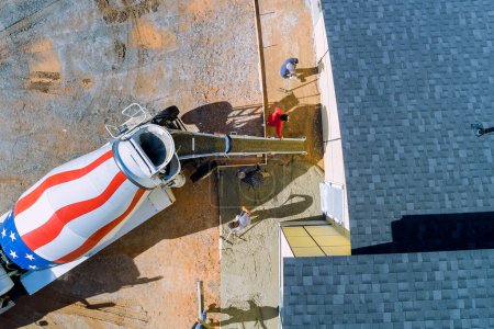 Photo for Concrete is being poured out by concrete mixing truck around new house for pavement - Royalty Free Image