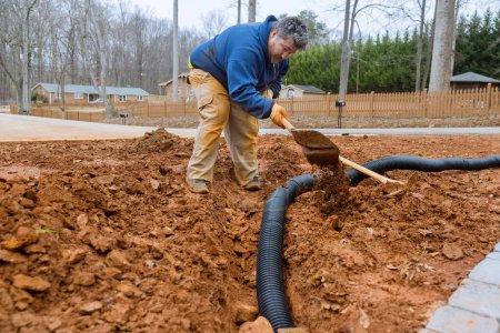 Photo for When rain is heavy worker digs trench to lay drainage pipes for rainwater during period of heavy rainfall. - Royalty Free Image