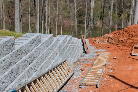 Téléchargez les photos : Construction d'un mur de bloc de soutènement sur une nouvelle propriété près d'une nouvelle maison - en image libre de droit