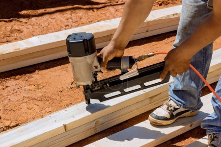 Téléchargez les photos : Utilisation d'un marteau à air entrepreneur clous poutres en bois pour encadrer la construction de logements pour le rendre plus fort - en image libre de droit