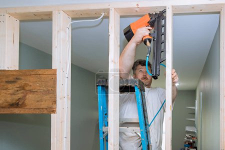 Téléchargez les photos : Utilisation d'un marteau pneumatique clous de constructeur poutres en bois aux cadres de logement pour la maison de construction - en image libre de droit